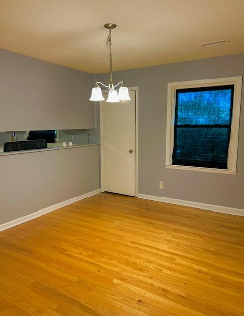 unfurnished room featuring light wood-type flooring, baseboards, visible vents, and a notable chandelier