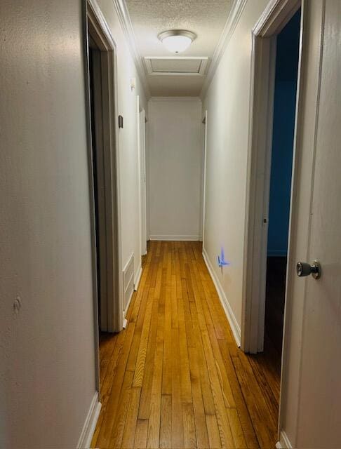 hallway with baseboards, ornamental molding, light wood-style flooring, attic access, and visible vents
