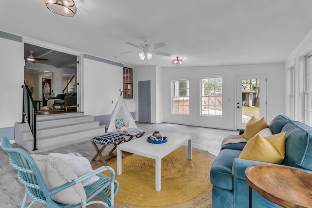 living area with stairway, wood finished floors, and a ceiling fan
