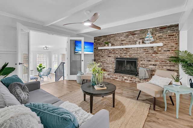living room with light wood-type flooring, beamed ceiling, a ceiling fan, and a brick fireplace