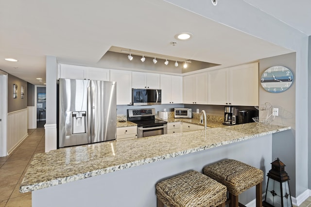 kitchen with light tile patterned floors, white cabinetry, stainless steel appliances, a kitchen bar, and kitchen peninsula