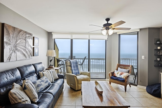 tiled living room with a water view, ceiling fan, and expansive windows