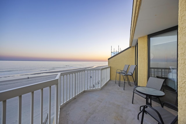 balcony at dusk featuring a water view and a view of the beach