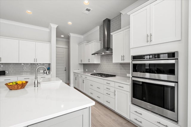 kitchen with white cabinets, stainless steel appliances, wall chimney exhaust hood, tasteful backsplash, and sink