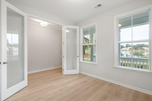 empty room with light hardwood / wood-style floors, a water view, and french doors