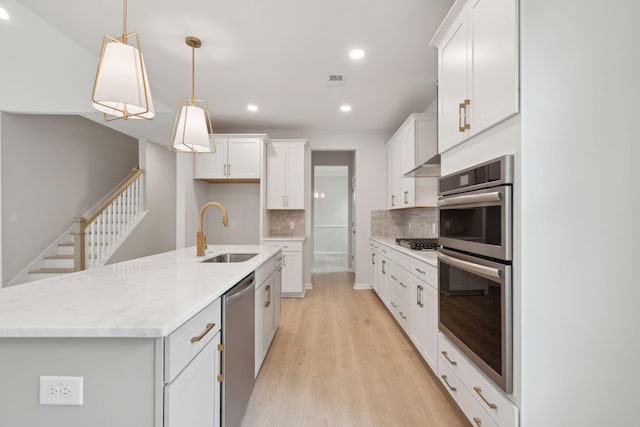 kitchen with decorative backsplash, sink, a center island with sink, white cabinets, and hanging light fixtures