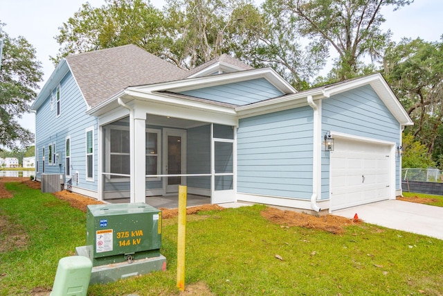 view of front of home with central AC unit, a garage, a front lawn, and a sunroom