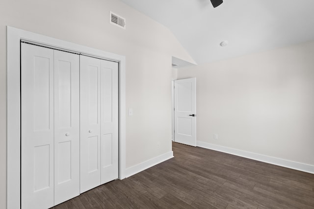 unfurnished bedroom featuring dark wood-style flooring, a closet, visible vents, vaulted ceiling, and baseboards