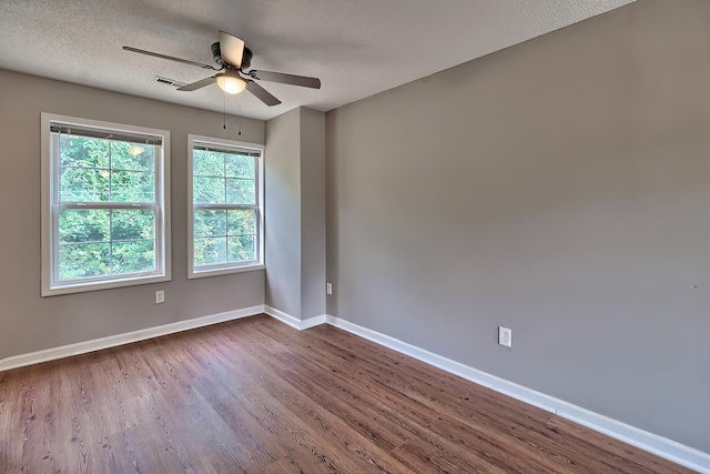 spare room featuring a textured ceiling, wood finished floors, visible vents, a ceiling fan, and baseboards