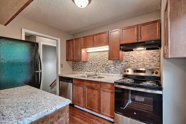 kitchen with under cabinet range hood, stainless steel appliances, dark wood-style flooring, a sink, and light countertops