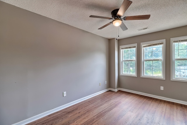 empty room with visible vents, a textured ceiling, baseboards, and wood finished floors