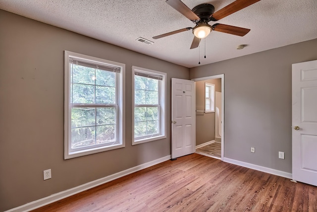 spare room featuring visible vents, a textured ceiling, baseboards, and wood finished floors