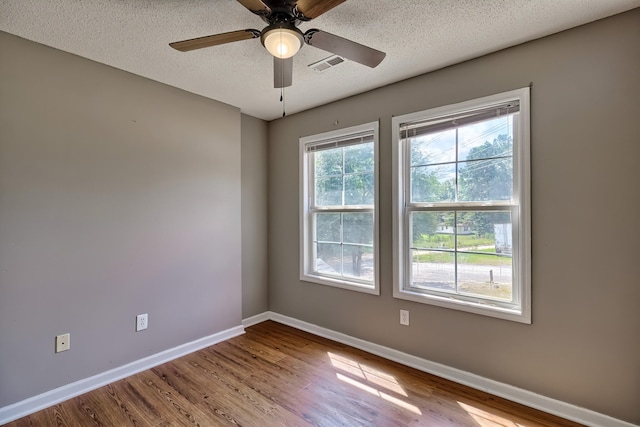 unfurnished room featuring a textured ceiling, ceiling fan, wood finished floors, visible vents, and baseboards