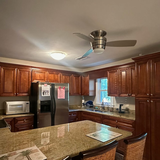 kitchen featuring light stone counters, sink, a kitchen bar, and stainless steel refrigerator with ice dispenser