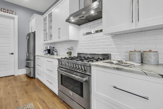 kitchen featuring white cabinets, wall chimney range hood, light stone countertops, light hardwood / wood-style floors, and stainless steel appliances