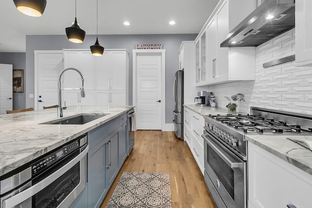 kitchen with stainless steel appliances, sink, wall chimney range hood, light hardwood / wood-style flooring, and white cabinetry