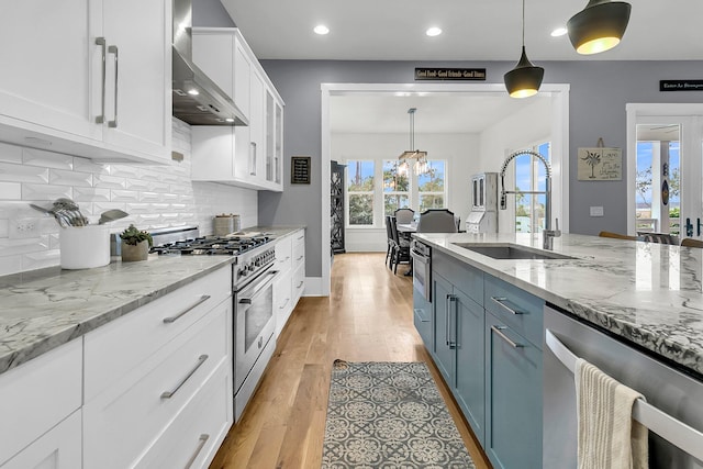 kitchen with white cabinetry, wall chimney range hood, pendant lighting, light hardwood / wood-style floors, and appliances with stainless steel finishes