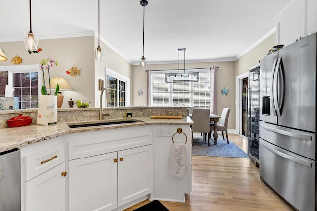 kitchen featuring light wood finished floors, appliances with stainless steel finishes, ornamental molding, white cabinetry, and a sink