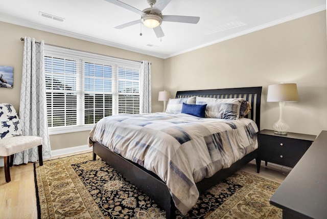 bedroom with crown molding, visible vents, ceiling fan, wood finished floors, and baseboards