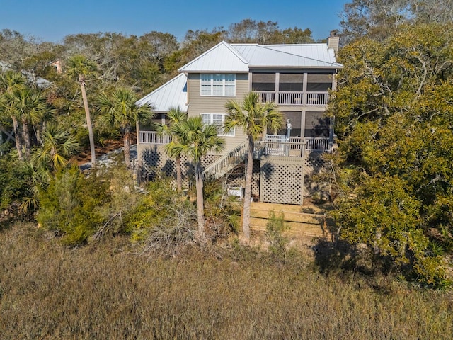 back of house featuring a standing seam roof, a chimney, stairway, and metal roof