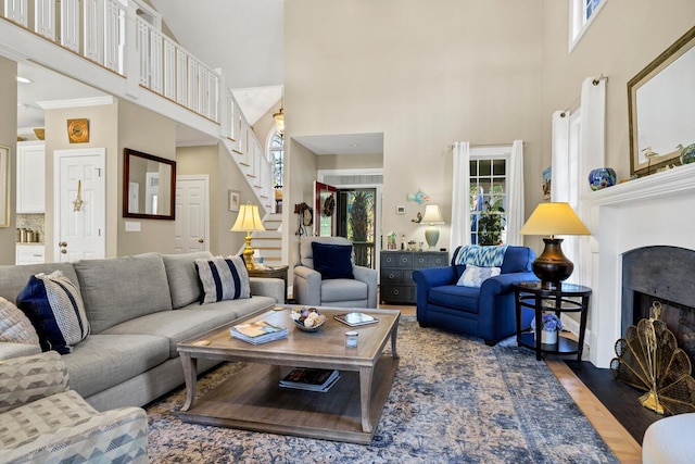 living area featuring a fireplace with flush hearth, stairway, a towering ceiling, and wood finished floors