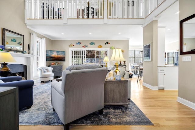 living area featuring light wood-style flooring, a fireplace, a towering ceiling, and baseboards