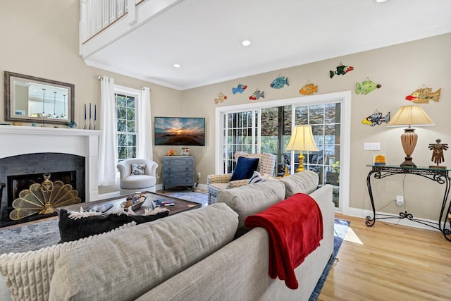 living area featuring light wood-style floors, a fireplace, baseboards, and crown molding