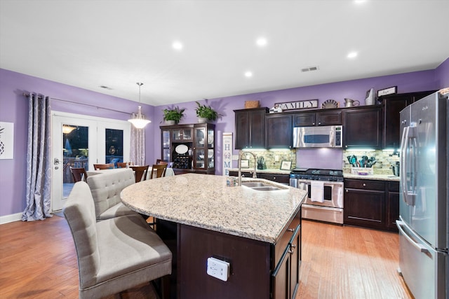 kitchen featuring visible vents, a breakfast bar area, stainless steel appliances, light wood-style floors, and a sink