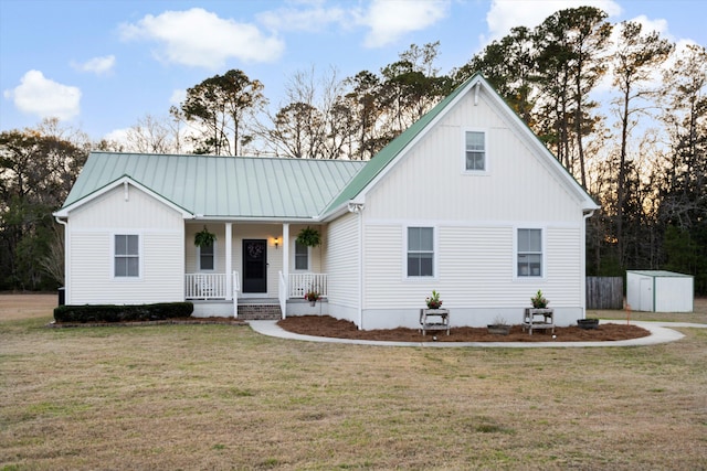 view of front of home featuring a storage unit, covered porch, a front yard, metal roof, and an outdoor structure