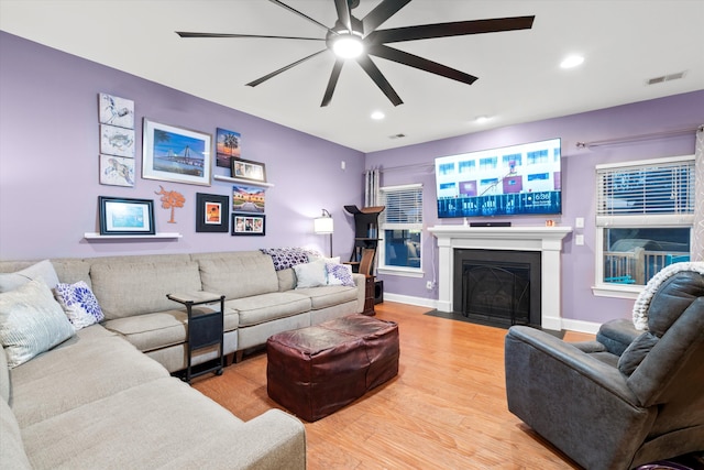 living area with light wood-style flooring, a fireplace with flush hearth, visible vents, baseboards, and a ceiling fan