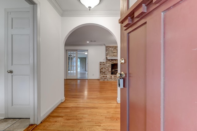 corridor with baseboards, light wood-style flooring, arched walkways, and crown molding