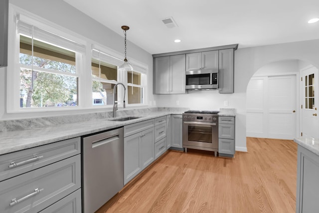 kitchen featuring visible vents, stainless steel appliances, gray cabinetry, light wood-type flooring, and a sink