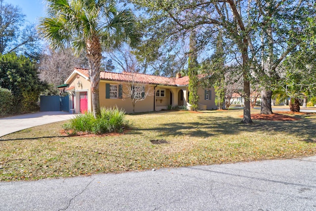 ranch-style home featuring driveway, a tile roof, an attached garage, a front yard, and stucco siding