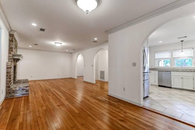 unfurnished living room featuring arched walkways, visible vents, a sink, and light wood finished floors