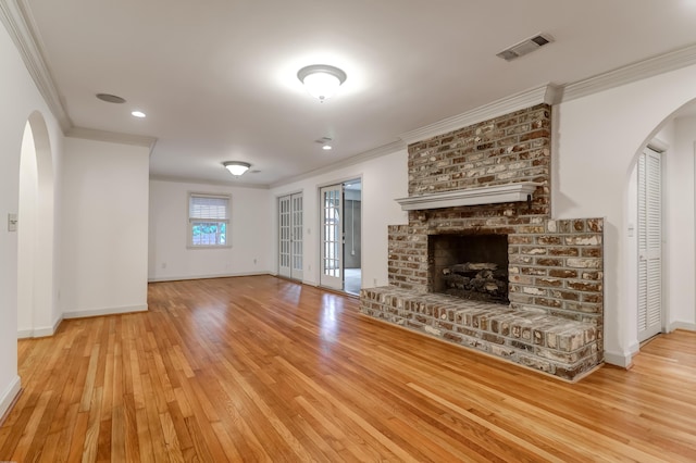 unfurnished living room featuring visible vents, arched walkways, ornamental molding, light wood-style floors, and a fireplace