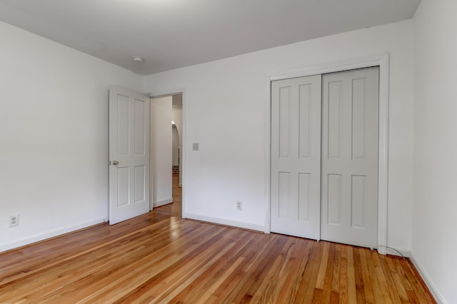 unfurnished bedroom with light wood-type flooring, arched walkways, a closet, and baseboards