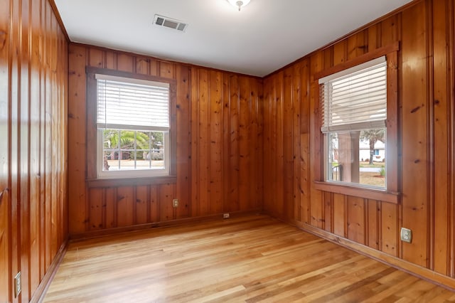 empty room featuring light wood-style floors, wooden walls, and visible vents