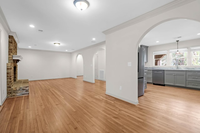 unfurnished living room with baseboards, visible vents, arched walkways, crown molding, and light wood-type flooring