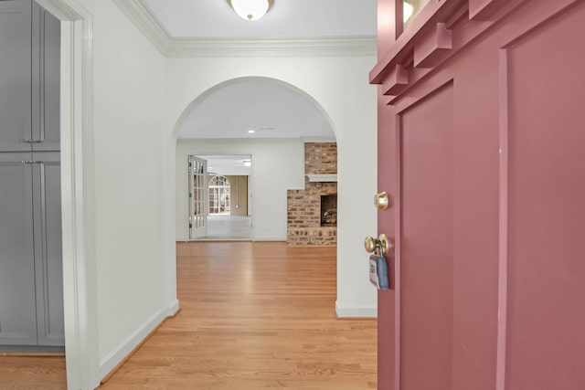 hallway featuring light wood-type flooring, crown molding, arched walkways, and baseboards