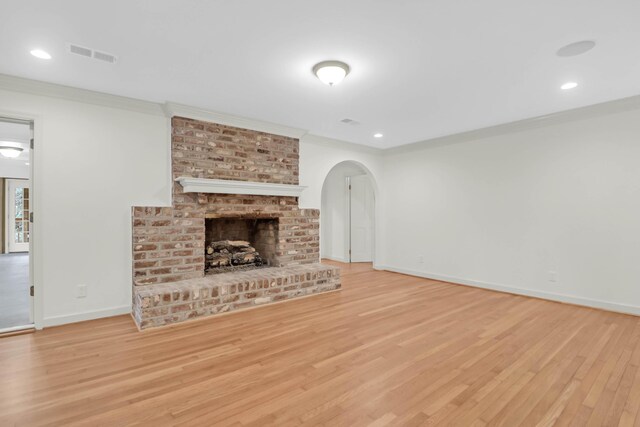 unfurnished living room featuring light wood finished floors, visible vents, arched walkways, and ornamental molding