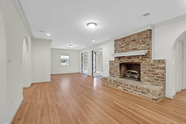 unfurnished living room featuring arched walkways, a brick fireplace, visible vents, and crown molding