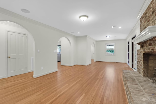 unfurnished living room featuring arched walkways, baseboards, light wood-type flooring, a brick fireplace, and crown molding