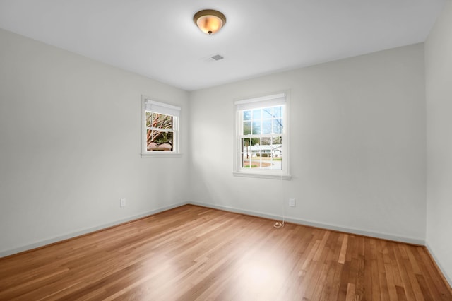 empty room featuring wood finished floors, visible vents, and baseboards