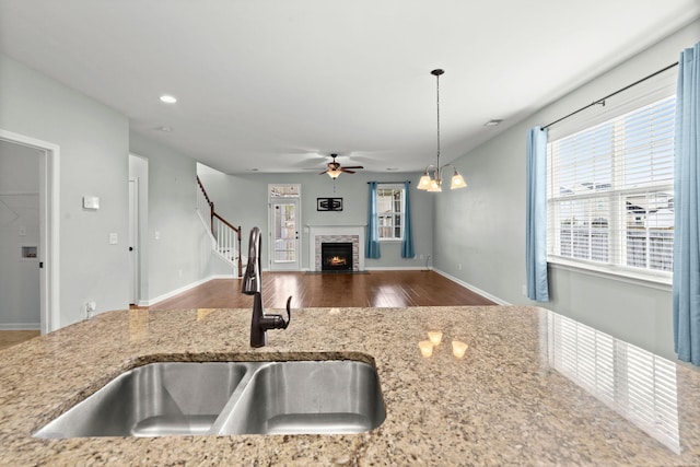 kitchen with pendant lighting, hardwood / wood-style floors, a stone fireplace, sink, and light stone counters