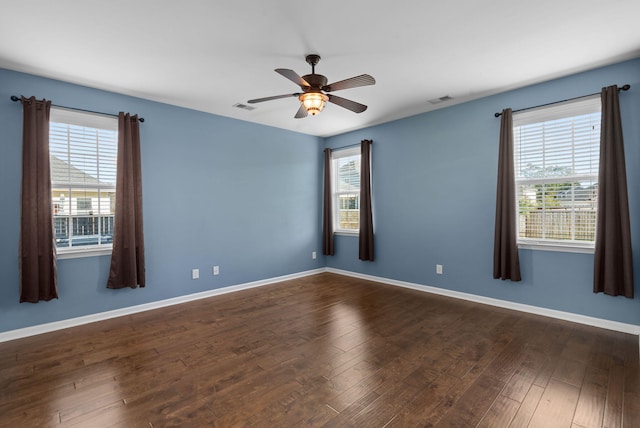 empty room featuring ceiling fan, dark wood-type flooring, and a wealth of natural light