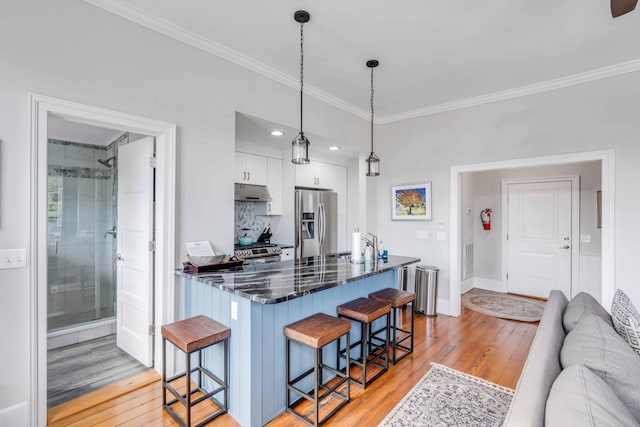 kitchen featuring pendant lighting, dark stone counters, white cabinets, a kitchen breakfast bar, and appliances with stainless steel finishes