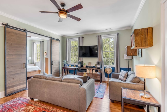 living room with a barn door, light hardwood / wood-style flooring, ceiling fan, and crown molding