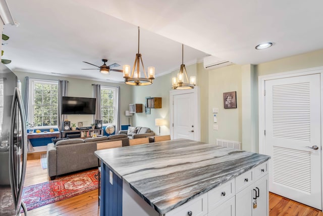 kitchen featuring stainless steel fridge, ceiling fan with notable chandelier, pendant lighting, white cabinets, and a kitchen island