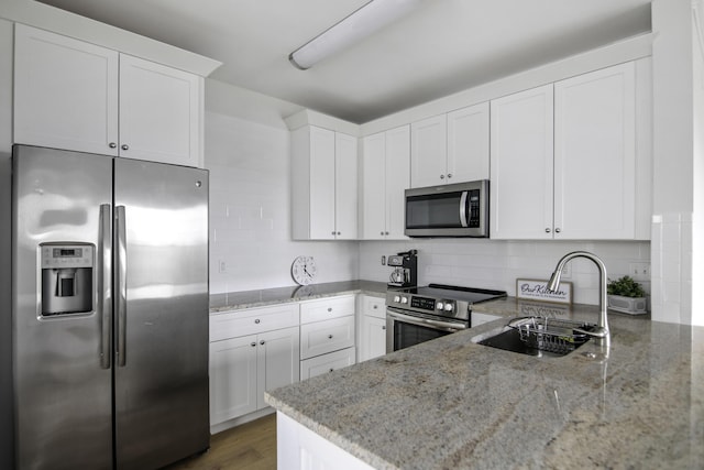 kitchen with stainless steel appliances, decorative backsplash, white cabinets, a sink, and light stone countertops