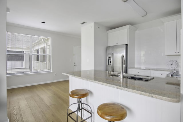 kitchen with stainless steel fridge, white cabinets, light wood-style flooring, light stone counters, and a sink